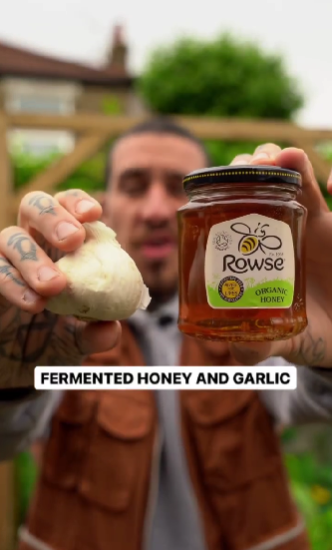 Alessandro Vitale aka Spicy Moustache, holding a bulb of garlic and a jar of honey